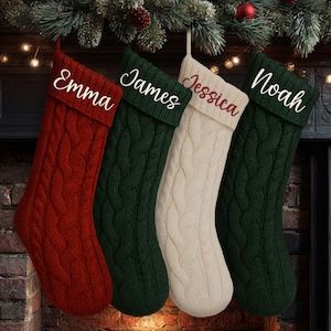 May include: Four cable-knit Christmas stockings in red, green, and cream hang from a fireplace. Each stocking is personalized with a name: Emma, James, Jessica, and Noah. Festive holiday decor.