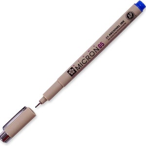 May include: A beige Micron 05 archival ink pen with a blue cap. The pen is labeled "#1 Archival Ink for Acid-Free Environments" and has a small flower logo.