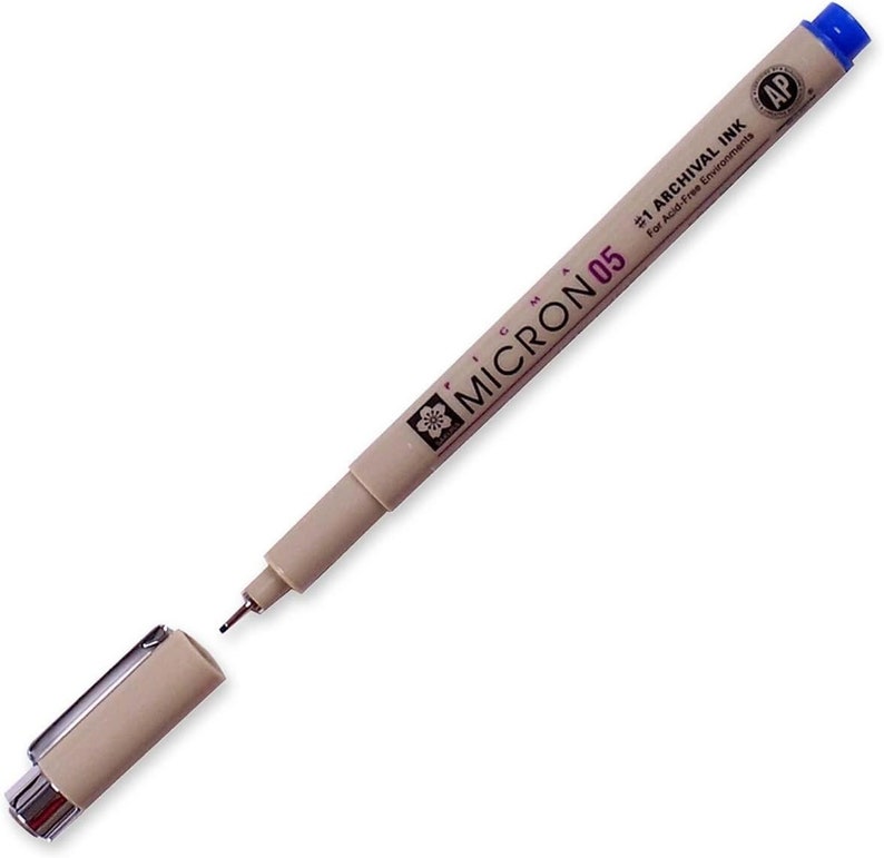 May include: A beige Micron 05 archival ink pen with a blue cap. The pen is labeled "#1 Archival Ink for Acid-Free Environments" and has a small flower logo.