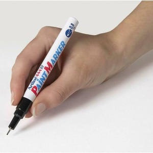 Puede incluir: Un marcador de pintura blanco con letras negras que dicen "Artline 444XF PAINT MARKER 0.8". El marcador está siendo sostenido por una mano.