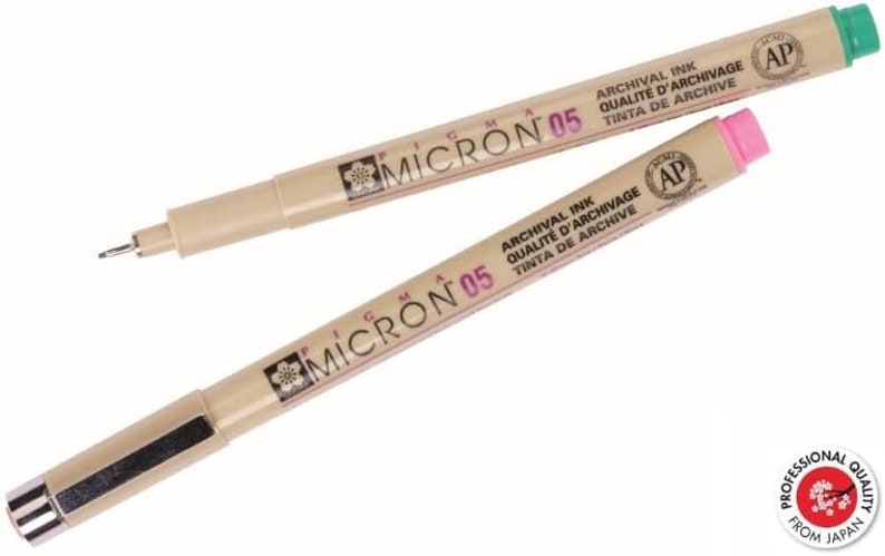 May include: Two brown and beige Micron 05 pens with black caps and green and pink caps. The pens have the text "Micron 05" and "Archival Ink Qualite d'Archive Tinta de Archive" printed on them. The pens are made in Japan.