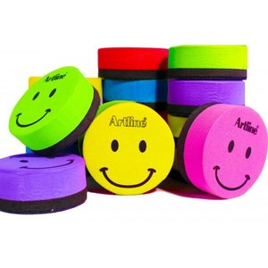 Könnte beinhalten: Ein Set runder, bunter Whiteboard-Radiergummis mit einem Smiley-Gesichtsdesign. Jeder Radiergummi hat eine schwarze Schaumstoffrückseite und den Aufdruck "Artline".