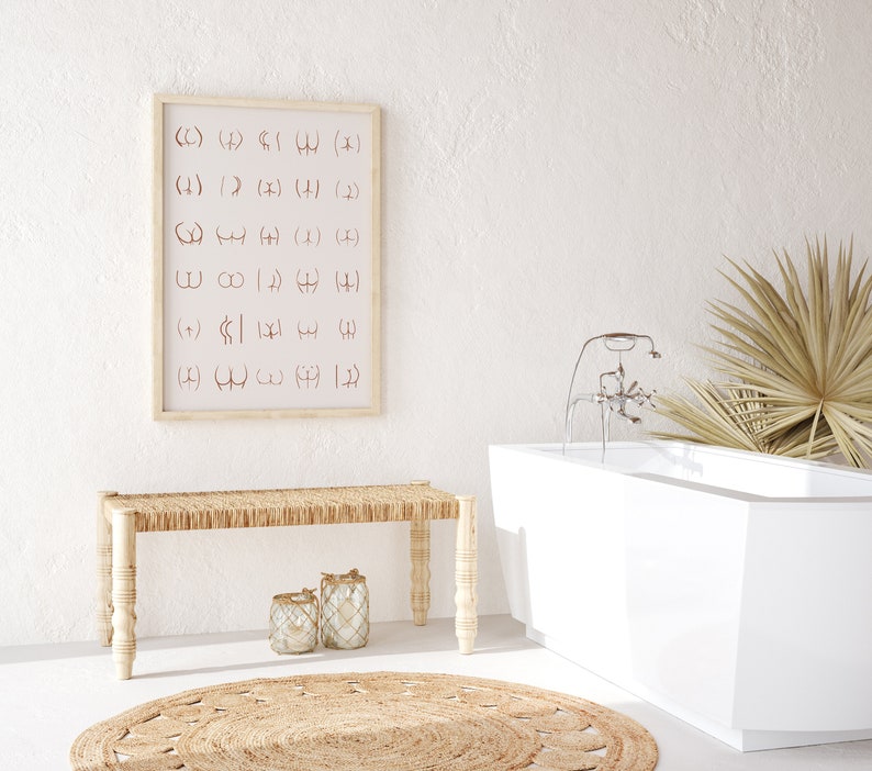 May include: A white bathtub with a chrome faucet and a palm leaf plant in the background. A wooden bench with a woven seat sits in front of a framed print with a pattern of abstract symbols.