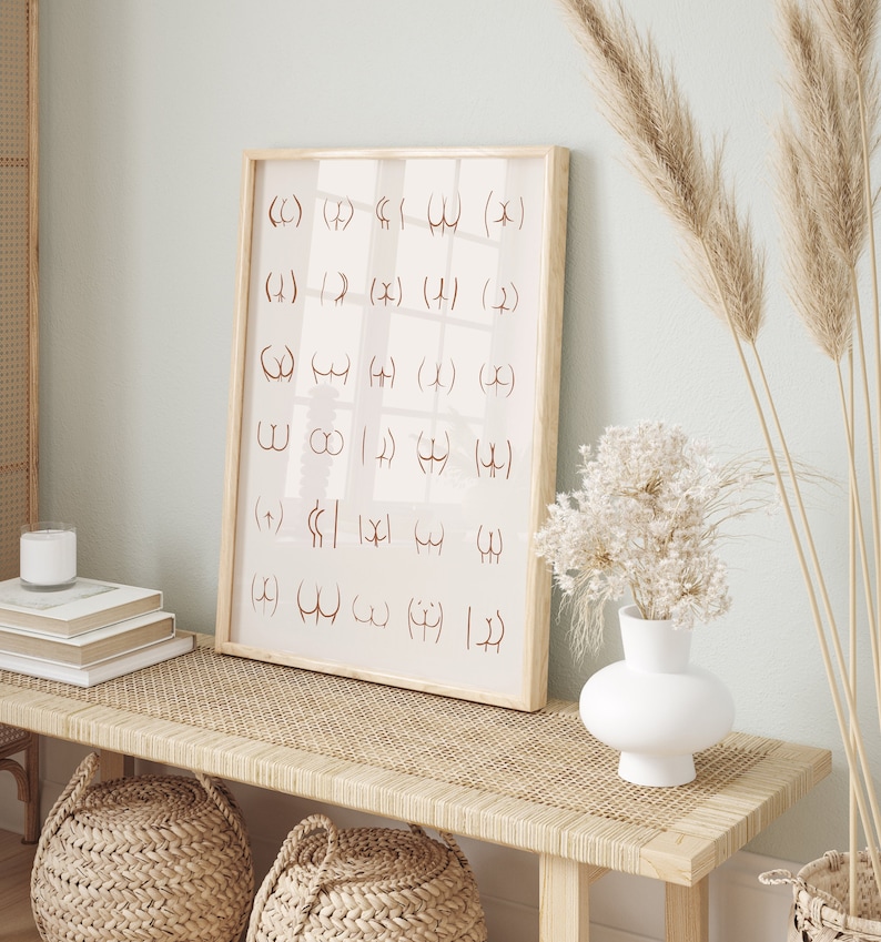 May include: A framed print with a light pink background and brown text. The text is a series of symbols and letters. The print is hanging on a wall above a light brown wooden bench with a woven rattan top. There are two woven baskets on the bench and a white vase with dried white flowers on the bench.