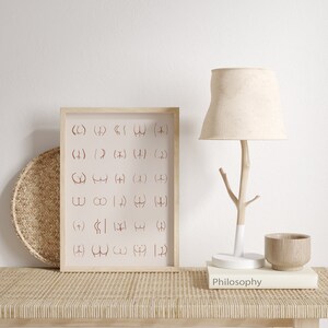 May include: A framed print with a white background and brown frame. The print features a grid of symbols in a reddish-brown color. The print is sitting on a light brown woven surface with a lamp, a book, and a wooden bowl.
