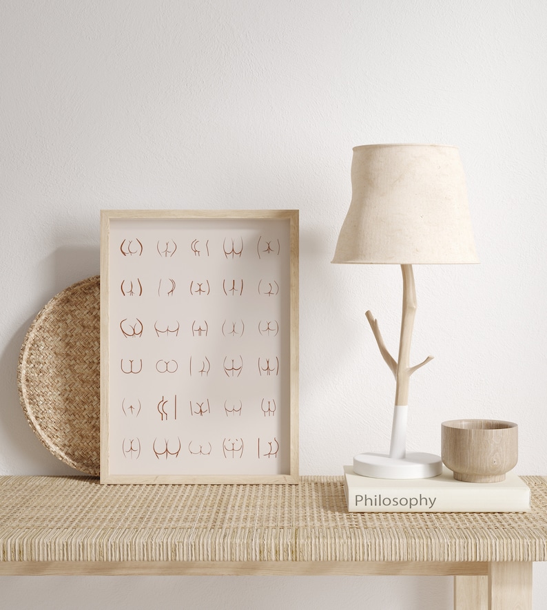 May include: A framed print with a white background and brown frame. The print features a grid of symbols in a reddish-brown color. The print is sitting on a light brown woven surface with a lamp, a book, and a wooden bowl.