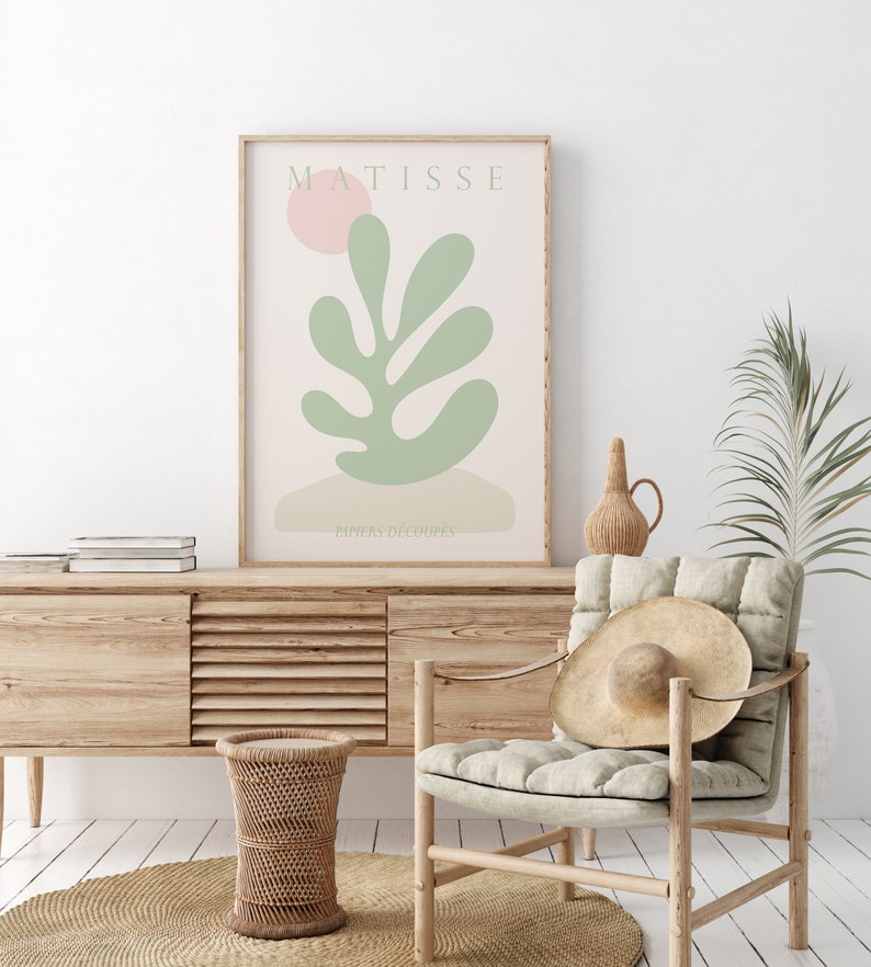 Op de afbeelding: Een ingelijst afdruk van een Matisse-kunstwerk met een groen blad en een roze cirkel op de achtergrond. De tekst "MATISSE" en "PAPIERS DECOUPES" is zichtbaar op de afdruk.