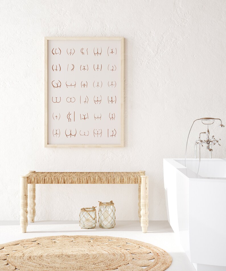 May include: A white bathroom with a white bathtub, a wooden bench with a woven seat, and a framed print with a series of symbols on a white background. Two glass lanterns with rope accents are on the floor in front of the bench.