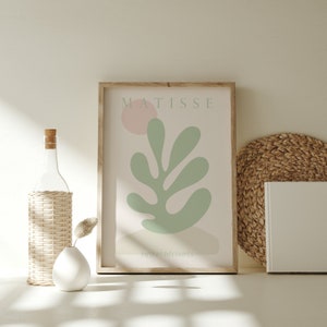 Op de afbeelding: Een ingelijste print van een Matisse kunstwerk met een groen blad met een roze cirkel op de achtergrond. De tekst "MATISSE" en "PAPIERS DECOUPES" staat op de print.