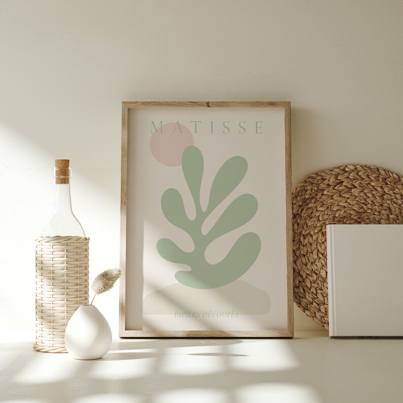Op de afbeelding: Een ingelijste print van een Matisse kunstwerk met een groen blad met een roze cirkel op de achtergrond. De tekst "MATISSE" en "PAPIERS DECOUPES" staat op de print.