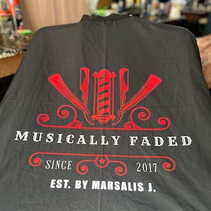 Può includere: Grembiule da barbiere nero con un logo rosso che dice "Musically Faded" con una stella e il testo "Since 2017 Est. By Marsalis J."