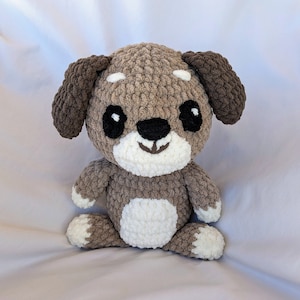 May include: A brown and white crocheted stuffed dog toy with black eyes and a smiling mouth.