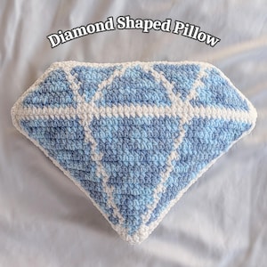 May include: A diamond-shaped pillow in shades of blue and white, crocheted with a textured stitch. The pillow has a geometric design and the text "Diamond Shaped Pillow" is above the pillow.
