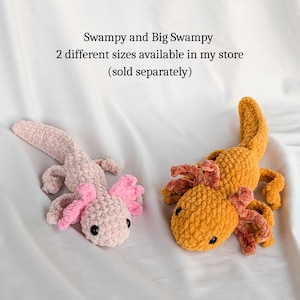 Puede incluir: Dos peluches de ajolote de ganchillo, uno rosa y otro naranja, se muestran sobre una superficie blanca. El ajolote rosa tiene branquias rosas y el naranja tiene branquias naranjas y rosas. El texto de arriba dice "Swampy and Big Swampy".