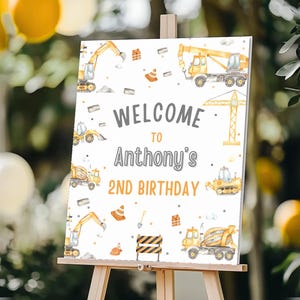 May include: A white welcome sign with a construction theme. The sign features a yellow excavator, a yellow dump truck, a yellow cement mixer, and a yellow crane. The sign says "Welcome to Anthony's 2nd Birthday".