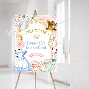 Może przedstawiać: Witamy na przyjęciu z okazji 1. urodzin Elizabeth w Onedeland, z motywem zaczerpniętym z Alicji w Krainie Czar&oacute;w. Tablica zawiera złotą ramę z r&oacute;żowo-niebieskim wzorem kwiatowym, zegar, filiżankę do herbaty i czajnik.