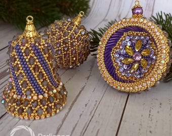 May include: Three decorative Christmas ornaments in gold, purple, and iridescent tones. The ornaments are shaped as a bell, a sphere, and a circle. They are embellished with beads and crystals, and have gold-coloured metal caps. The ornaments are displayed on a wooden surface.