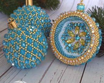 May include: Three handcrafted Christmas baubles. Two are spherical, covered in turquoise beads with gold accents. The third is a flat disc with a turquoise and gold beaded border, and a central floral design with yellow and turquoise gems. The baubles have gold caps.