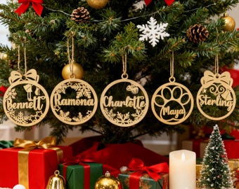 May include: Wooden Christmas tree ornaments with names: Bennett, Ramona, Charlotte, Maya, and Sterling. Each ornament is a circular design with intricate cutouts and a name. The ornaments hang from a Christmas tree decorated with red bows and gold ornaments.