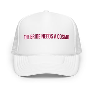 May include: White trucker hat with a pink embroidered design that says "The Bride Needs a Cosmo".