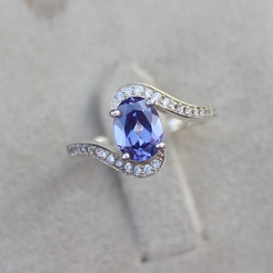 Puede incluir: Un anillo de plata con una gran piedra preciosa ovalada de color púrpura rodeada de pequeñas piedras preciosas transparentes.