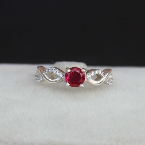 May include: A silver ring with a red gemstone and small clear gemstones set in a twisted band.