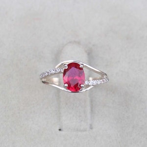 May include: A silver ring with a red oval gemstone and smaller clear gemstones set in the band.