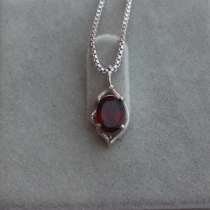 May include: A silver chain necklace with a pendant featuring a red oval gemstone set in a silver filigree design.