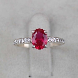 May include: A silver ring with a red oval gemstone surrounded by smaller white gemstones.