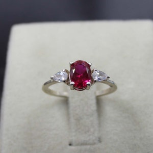 May include: A silver ring with a large oval-shaped red gemstone and two smaller pear-shaped clear gemstones.