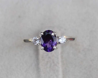 Puede incluir: Un anillo de plata con una gran amatista ovalada y dos diamantes redondos más pequeños a cada lado.