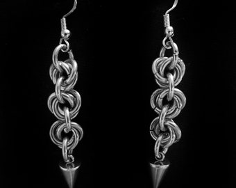 May include: A pair of silver earrings with a chain link design and a pointed tip. The earrings are hanging against a black background.