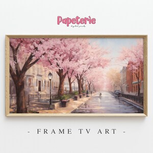 May include: A framed digital print of a street lined with cherry blossom trees in full bloom. The artwork features a wet street reflecting the sky and buildings, with figures walking in the distance. The text "Papeterie" and "- FRAME TV ART -" are visible.