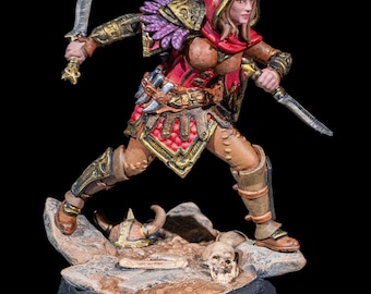May include: A painted miniature figurine of a female elf warrior wearing a red hooded cloak and holding two daggers. The figurine is standing on a base with a skull and bones.