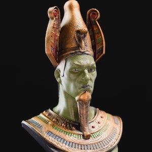 May include: A green and gold bust of an Egyptian pharaoh wearing a traditional headdress with intricate details. The bust is made of a smooth, painted material and features a detailed face and beard.