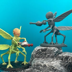 Peut inclure: Deux figurines d'extraterrestres vertes et grises avec des ailes et des armes, debout sur des rochers gris sur un fond bleu.