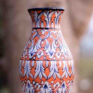 Może przedstawiać: Ceramiczny wazon z niebiesko-białym wzorem kwiatowym na pomarańczowym tle. Wazon ma okrągły korpus i wąską szyjkę.