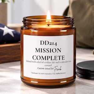 May include: A lit soy wax candle in an amber glass jar with a white label reading DD214 MISSION COMPLETE, Infused with relief of civilian life and a calendar you control, Custom-issued for Frank, Handmade USA 100% Natural Soy Wax KaliBayElements.