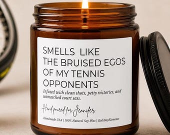May include: A lit brown glass jar candle with a black lid. The candle has a white label with the text "SMELLS LIKE THE BRUISED EGOS OF MY TENNIS OPPONENTS". The candle is handmade with natural soy wax.