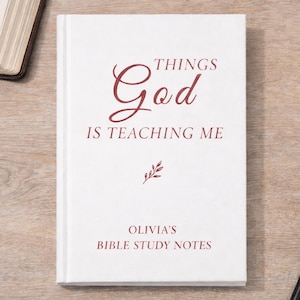 May include: A white Bible study notebook with the text "THINGS God IS TEACHING ME" in burgundy script. The notebook also includes the name "Olivia's" and "BIBLE STUDY NOTES". A rosary and a pen are also visible.