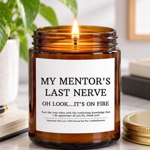 Può includere: Una candela accesa in un barattolo di vetro ambrato con un'etichetta bianca che riporta il testo nero: MY MENTOR'S LAST NERVE OH LOOK...IT'S ON FIRE. Sotto, un testo più piccolo recita: Feel the cozy vibes with the comforting knowledge that I do appreciate all you do, thank you! Handmade With Love | 100% Natural Soy Wax | KaliBayElements.