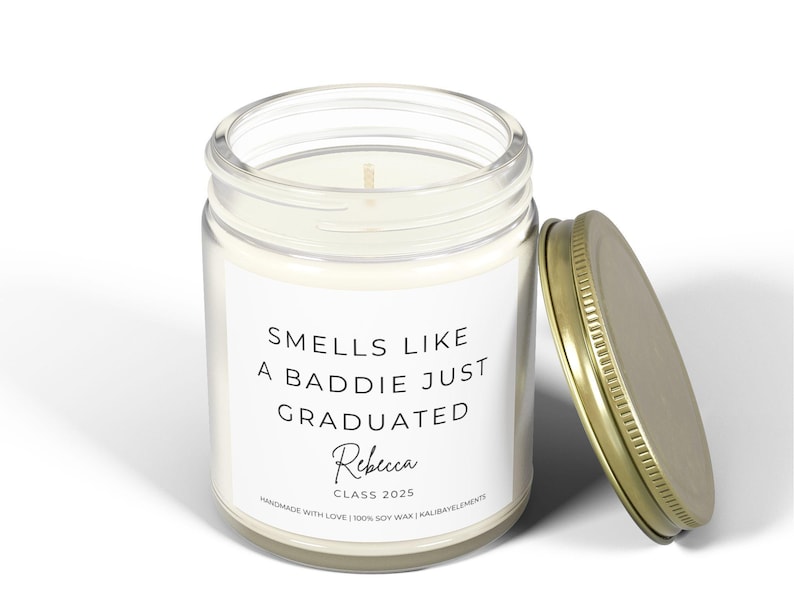 A white candle jar with a gold lid. The label reads "Smells like a baddie just graduated" with the name "Rebecca" and "Class 2025" underneath. The candle is handmade with 100% soy wax.