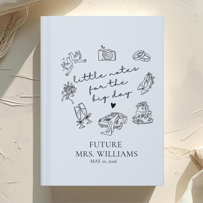 May include: A white wedding journal with black line art illustrations of wedding-related icons, including rings, a camera, and a cake. The text "little notes for the big day" is featured, along with the names "FUTURE MRS. WILLIAMS" and the date "MAY 10, 2026".