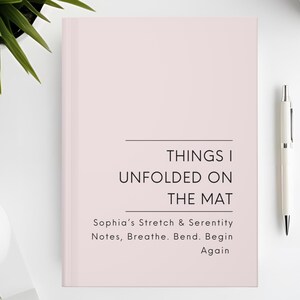 以下が含まれることがあります： 「THINGS I UNFOLDED ON THE MAT」というタイトルの薄いピンク色のジャーナル。テキストは「Sophia's Stretch & Serenity Notes, Breathe. Bend. Begin Again」と書かれています。白いペンとコーヒーカップが白い表面にあります。