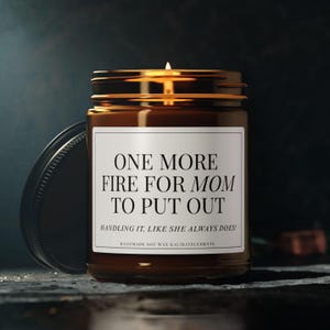 May include: A brown glass jar candle with a gold lid and a white label. The label reads "ONE MORE FIRE FOR MOM TO PUT OUT. HANDLING IT, LIKE SHE ALWAYS DOES!" The candle is handmade soy wax.
