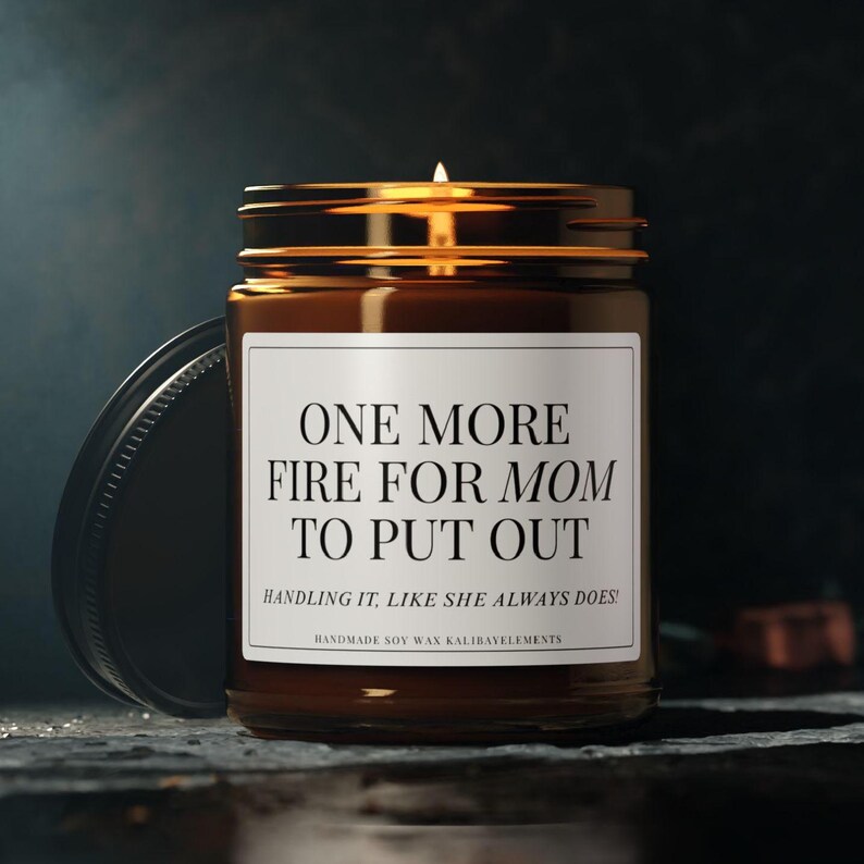 May include: A brown glass jar candle with a gold lid and a white label. The label reads "ONE MORE FIRE FOR MOM TO PUT OUT. HANDLING IT, LIKE SHE ALWAYS DOES!" The candle is handmade soy wax.