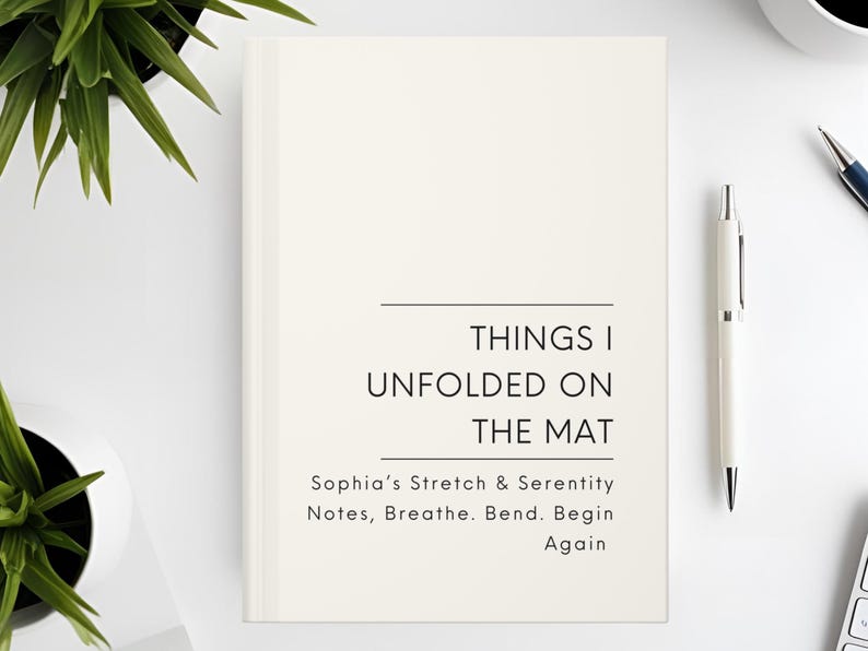 以下が含まれることがあります： 「THINGS I UNFOLDED ON THE MAT」と「Sophia's Stretch & Serenity Notes, Breathe. Bend. Begin Again」の文字が入ったクリーム色のジャーナル。白いペンと植物が白い表面に置かれています。