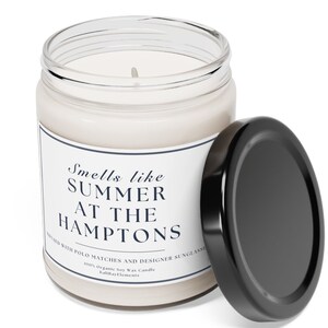 以下が含まれることがあります： 黒い蓋のついたガラス製のキャンドルが入った瓶。ラベルには「Smells like SUMMER AT THE HAMPTONS」と「Infused with Polo Matches and Designer Sunglasses」と書かれている。100%オーガニックソイワックスキャンドル。Saltwater Elements.