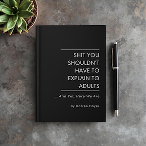 May include: A black book with the title "SHIT YOU SHOULDN'T HAVE TO EXPLAIN TO ADULTS" and the author's name, Darren Hayes. A black pen rests beside the book on a gray surface. A small potted succulent is in the upper left corner.