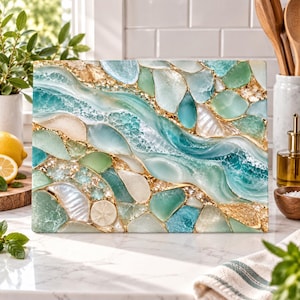 May include: A rectangular chopping board featuring a mosaic design of smooth sea glass, polished stones, and iridescent shells in shades of teal, aqua, mint green, and cream, all set within gold-toned resin veins that mimic flowing water.